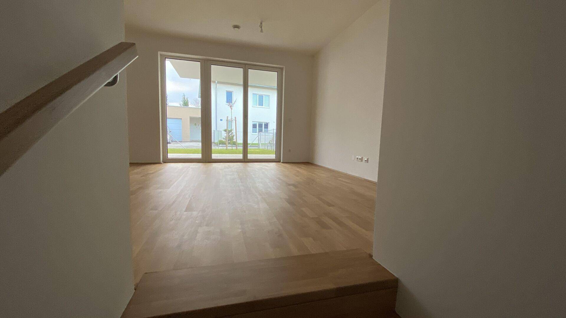 Blick vom Treppenbereich in den hellen Wohnraum mit Holzboden und Gartenzugang.