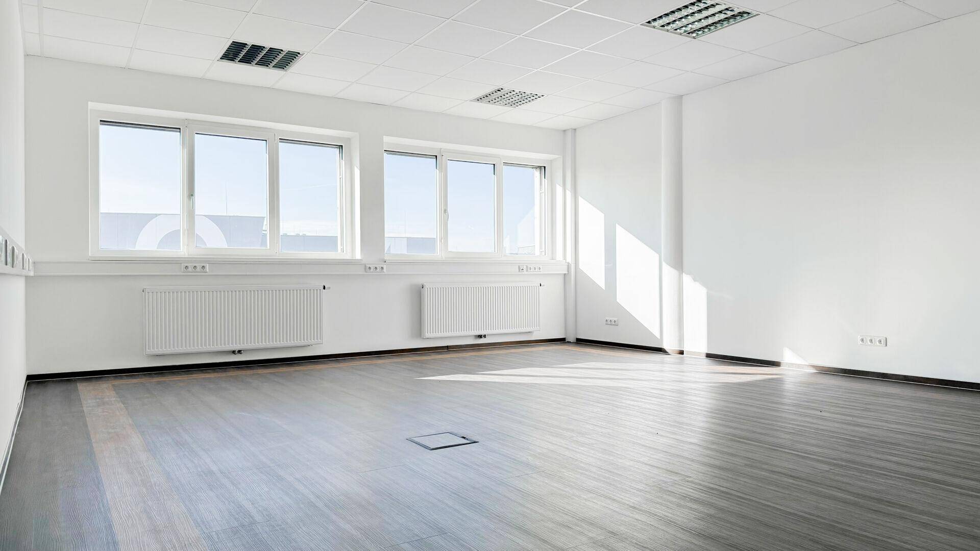 Geräumiger, heller Büroraum mit großen Fenstern und dunklem Laminatboden, bereit zur individuellen Gestaltung.