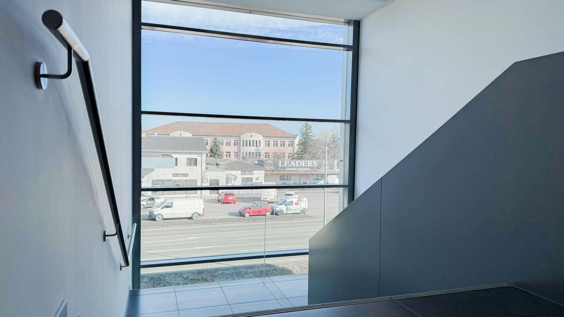 Modernes Treppenhaus mit großen Fenstern, die einen Blick auf die Straße und Gebäude bieten.