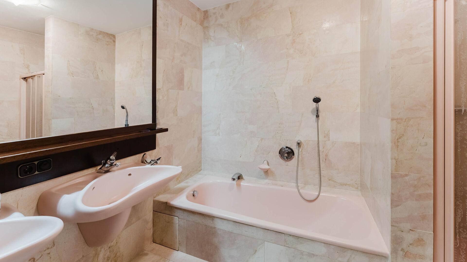 Badezimmer mit rosa Badewanne, Doppelwaschbecken und Marmorfliesen.