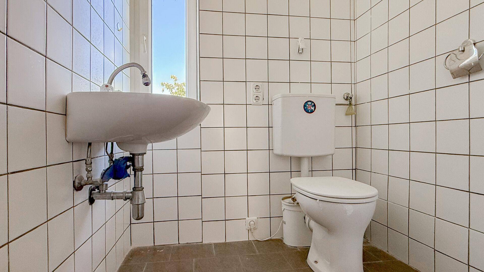 Kleines WC mit Toilette, wandmontiertem Waschbecken und weißen Fliesen mit dunklen Fugen.