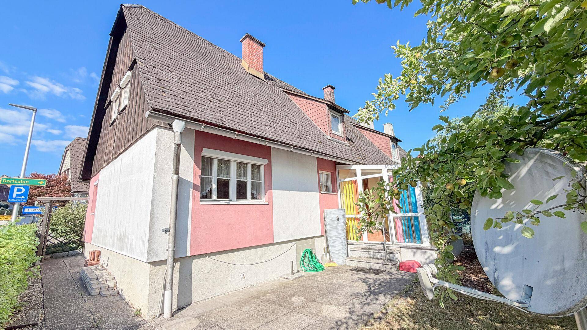 Seitenansicht des Hauses mit gepflastertem Bereich, Gartenschlauch und Satellitenschüssel.
