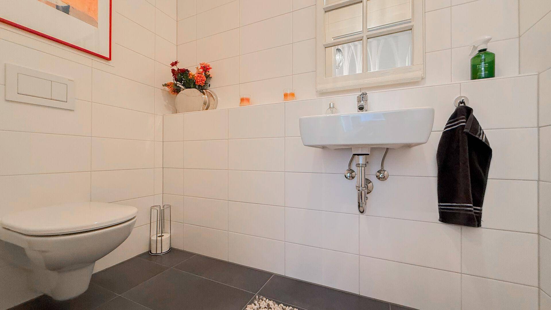 Helles Gäste-WC mit wandhängender Toilette, kleinem Waschbecken und modernen Fliesen.