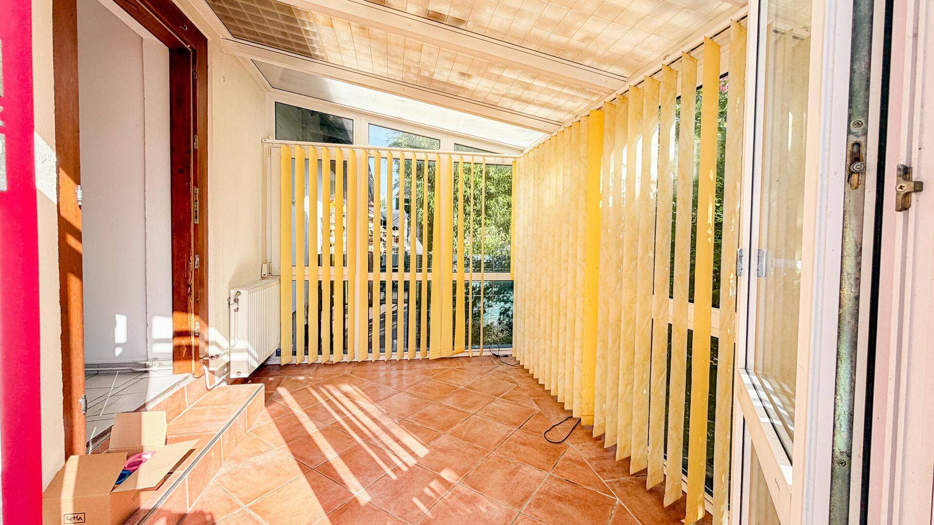 Heller Wintergarten mit Terrakotta-Fliesenboden und vertikalen Jalousien für viel Tageslicht.