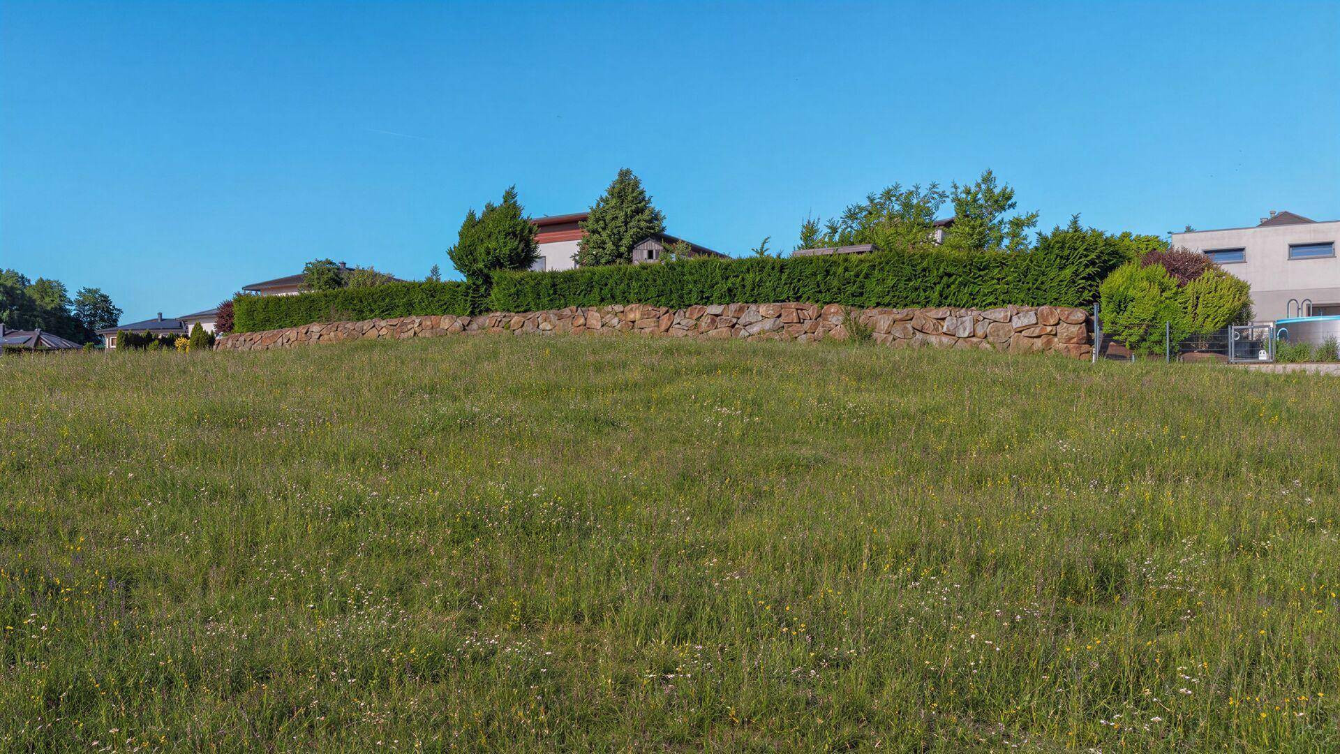 Weitläufiges Wiesengrundstück mit angrenzenden Häusern und einer Natursteinmauer.