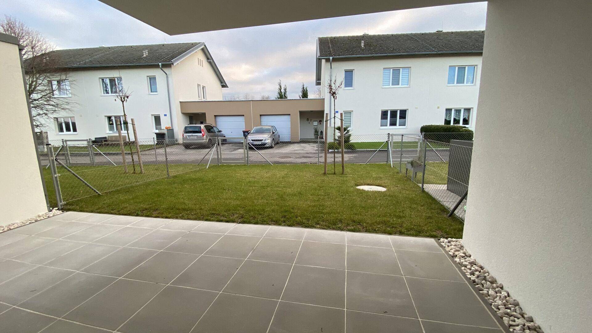 Gepflasterte Terrasse mit kleinem Rasenbereich und Blick auf die Nachbarschaft.