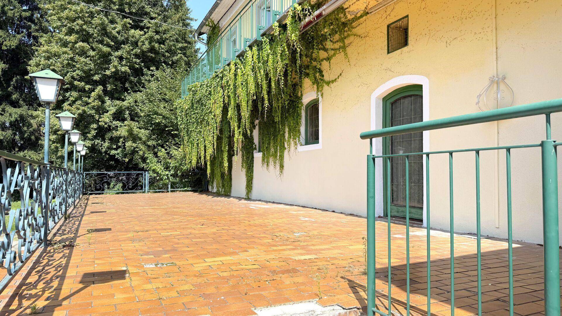 Große, geflieste Terrasse mit schmiedeeisernem Geländer und üppiger Begrünung.