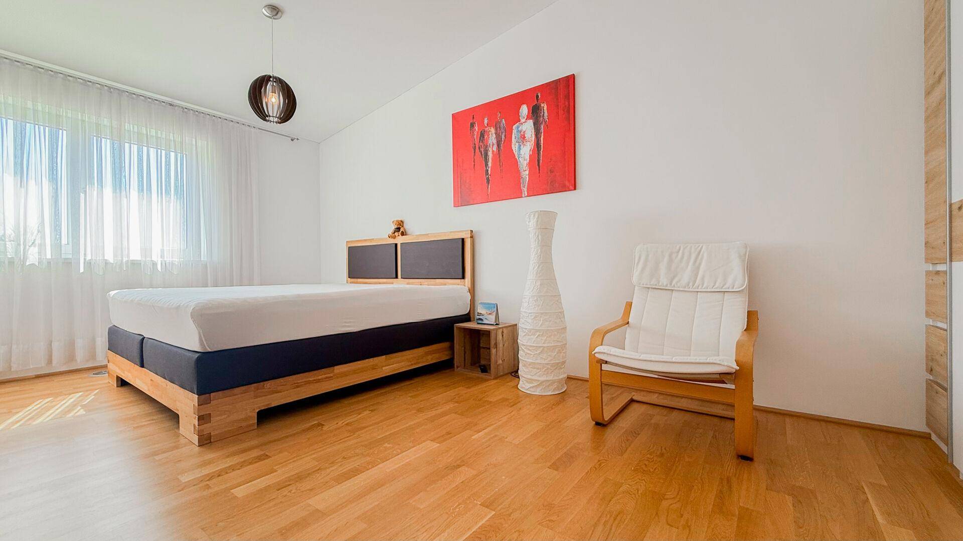 Ruhiges Schlafzimmer mit Holzbett, hellen Wänden und großem Fenster für viel Tageslicht.