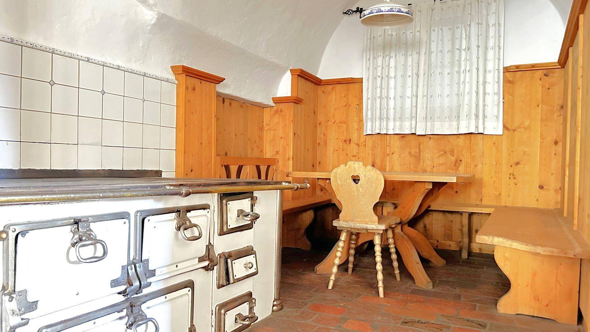 Rustikale Küche mit traditionellem Holzherd, Holzbänken und gefliesten Wänden.