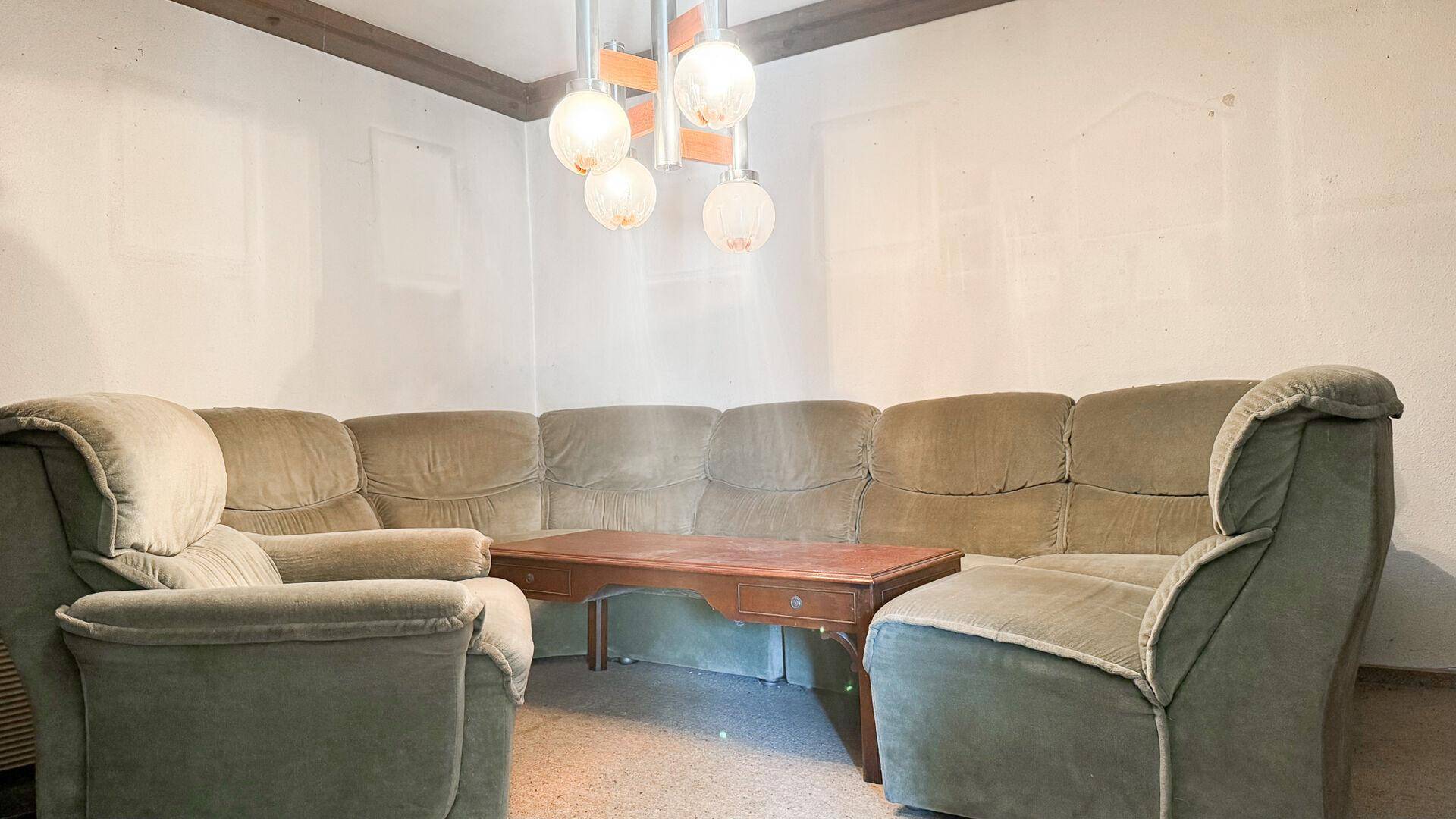 Wohnzimmer mit großer Eckcouch und Couchtisch, beleuchtet von einer modernen Deckenleuchte.