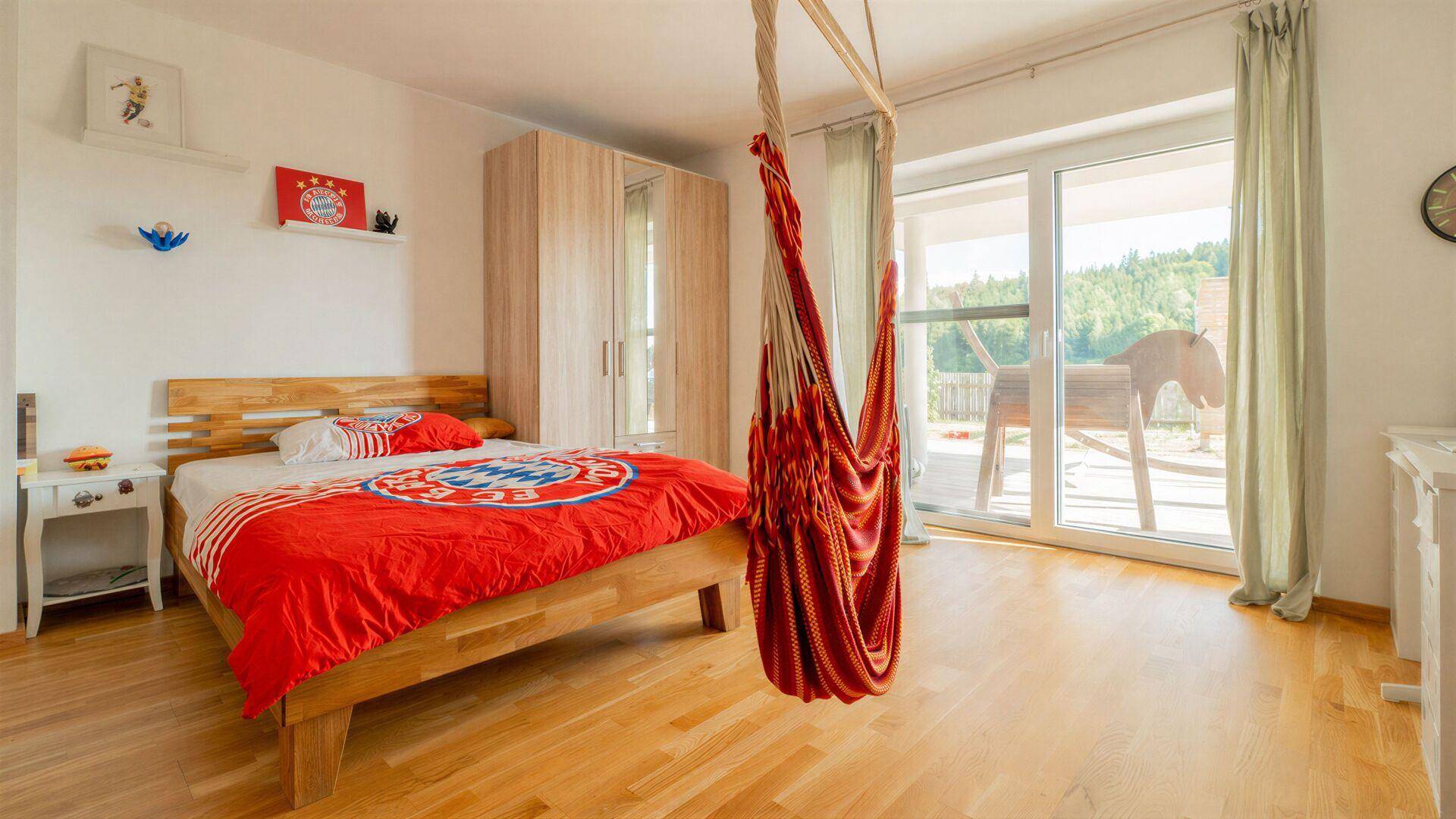 Helles Schlafzimmer mit Holzboden, Zugang zum Balkon und einem Hängesessel, gemütlich eingerichtet.