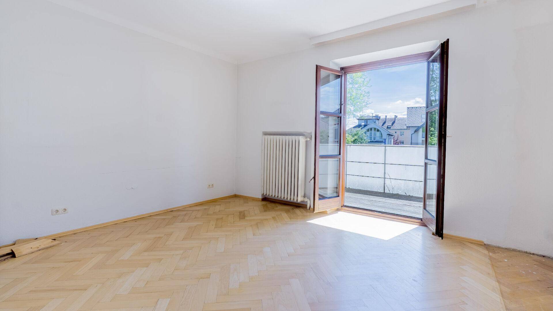 Helles Schlafzimmer mit Fischgrätparkett und Zugang zu einem Balkon.