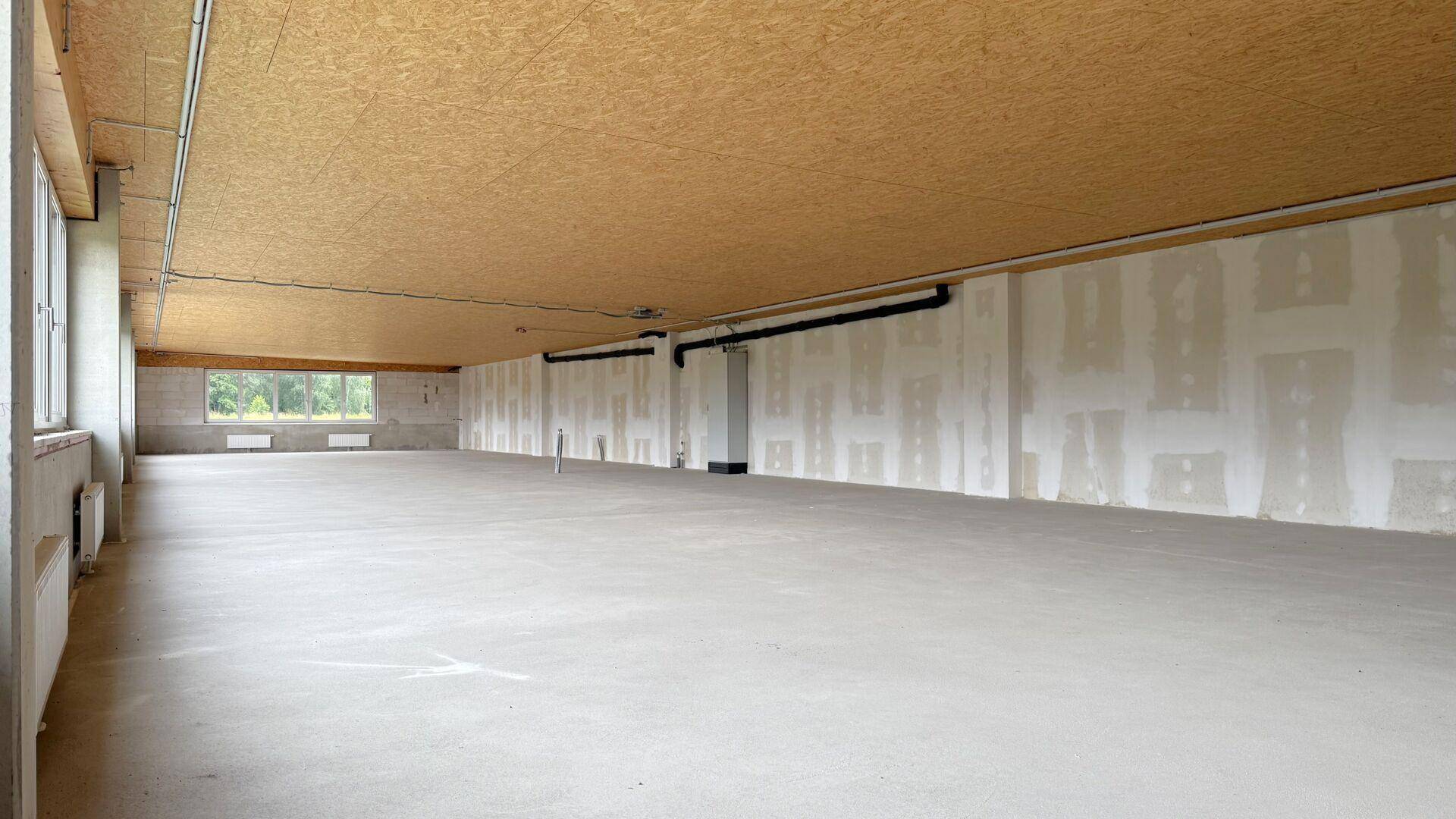 Geräumiger Gewerberaum im Rohbauzustand mit großen Fenstern und Blick auf die umliegende Natur.
