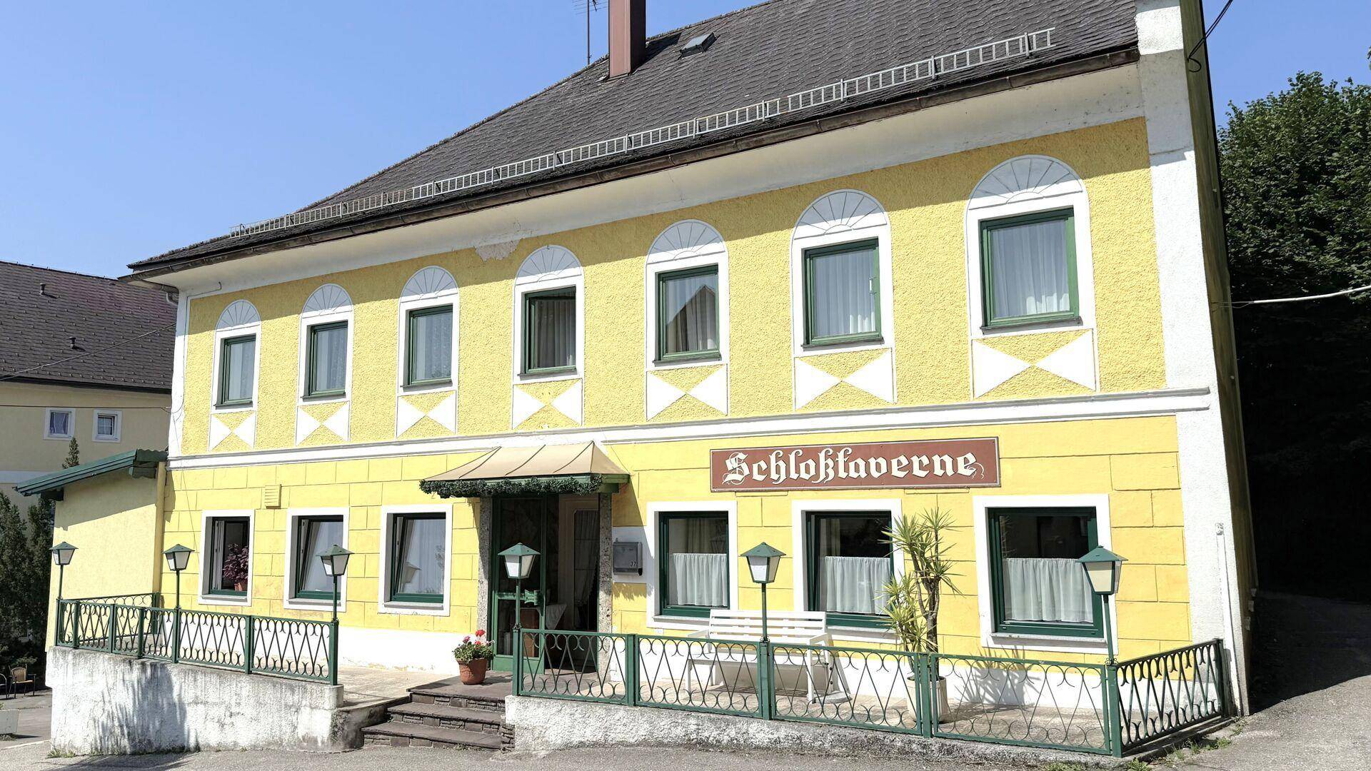 Vorderansicht des historischen Gebäudes mit gelber Fassade, grünen Fensterrahmen und dem Schriftzug "Schloßtaverne".