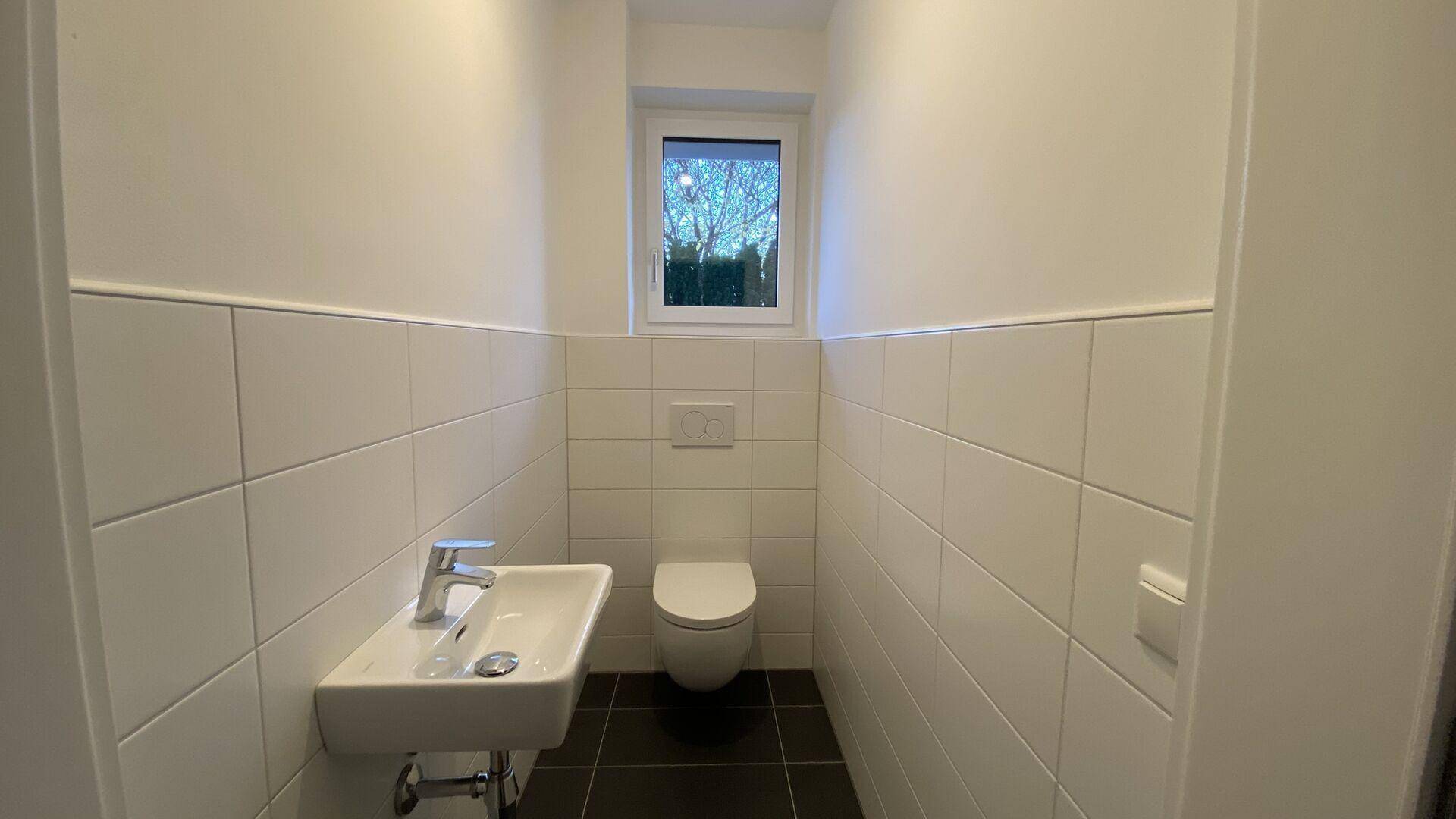 Modernes Gäste-WC mit Wand-WC, kleinem Waschbecken und Fenster für Tageslicht.
