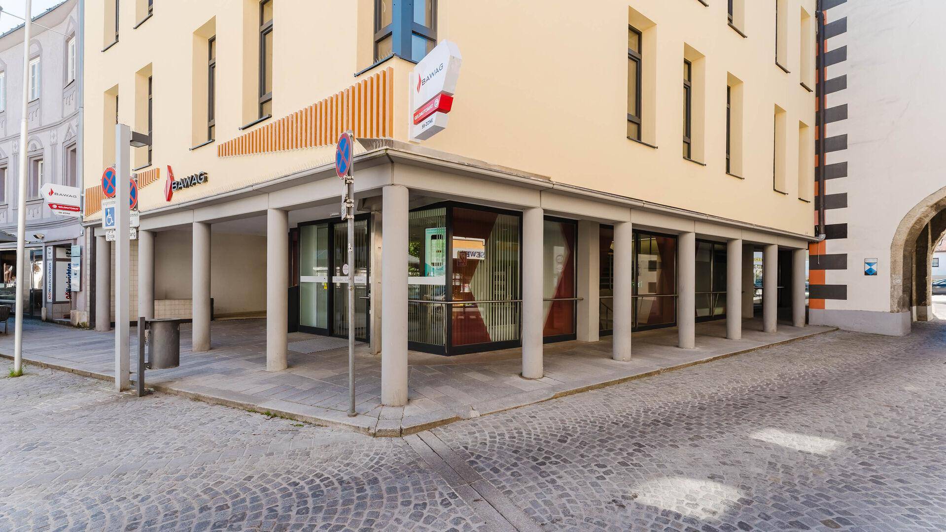 Eckgebäude mit Säulen und großen Schaufenstern an einer gepflasterten Straße in der Stadt.