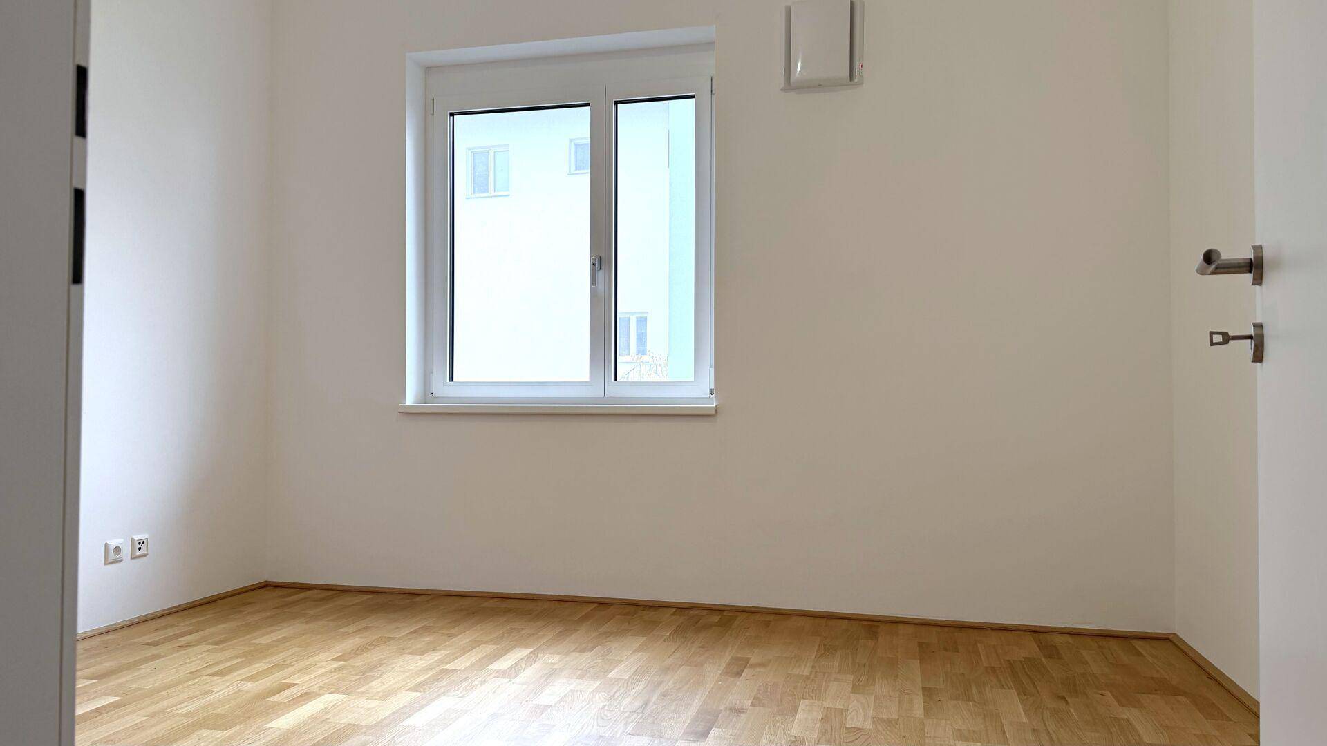 Helles Schlafzimmer mit Parkettboden und einem großen Fenster, das den Raum mit Licht füllt.