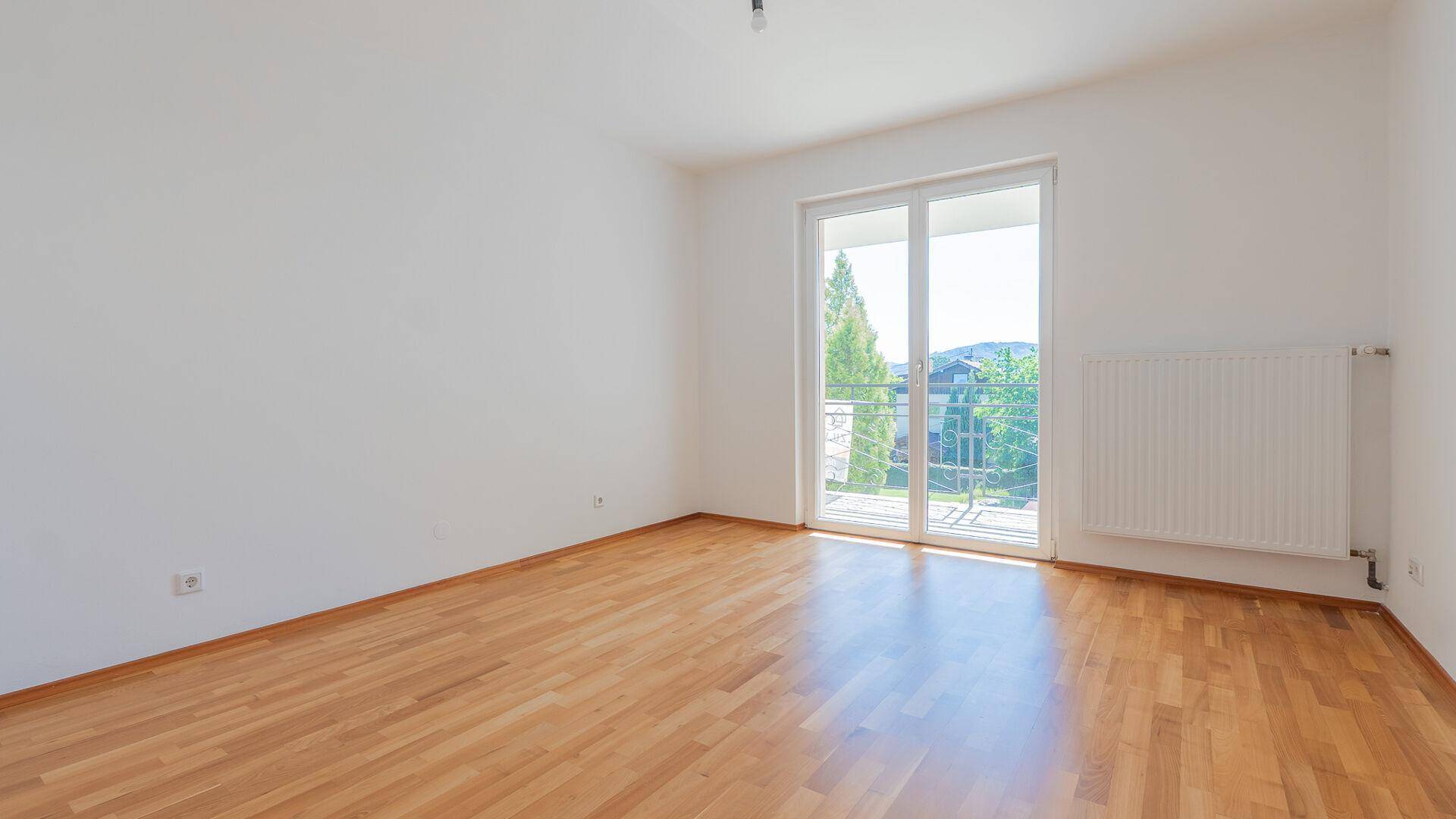 Helles Schlafzimmer mit Parkettboden und Balkonzugang durch eine große Glastür.