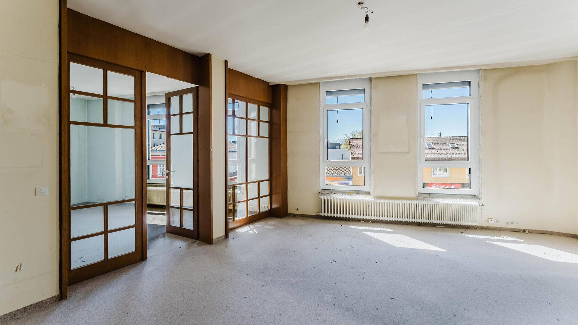 Geräumiger, heller Raum mit Holztüren und großen Fenstern, ideal für eine flexible Nutzung.