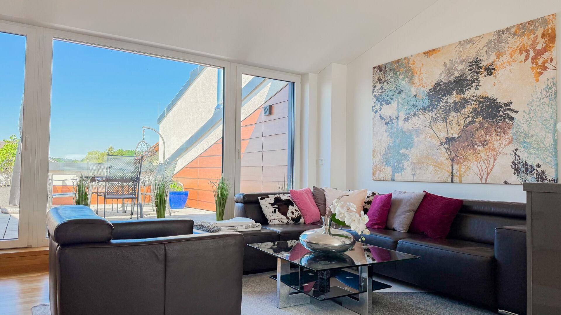 Gemütliches Wohnzimmer mit Ledersofa, Kunstwerk und direktem Zugang zur sonnigen Dachterrasse.