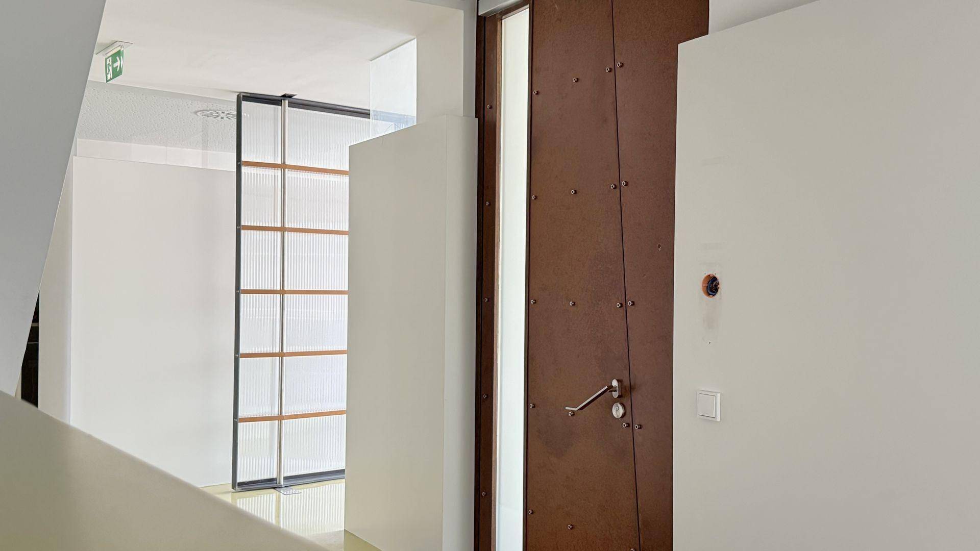 Heller Flur mit einer markanten braunen Tür, weißen Wänden und einer modernen Glasabtrennung mit Holzdetails.