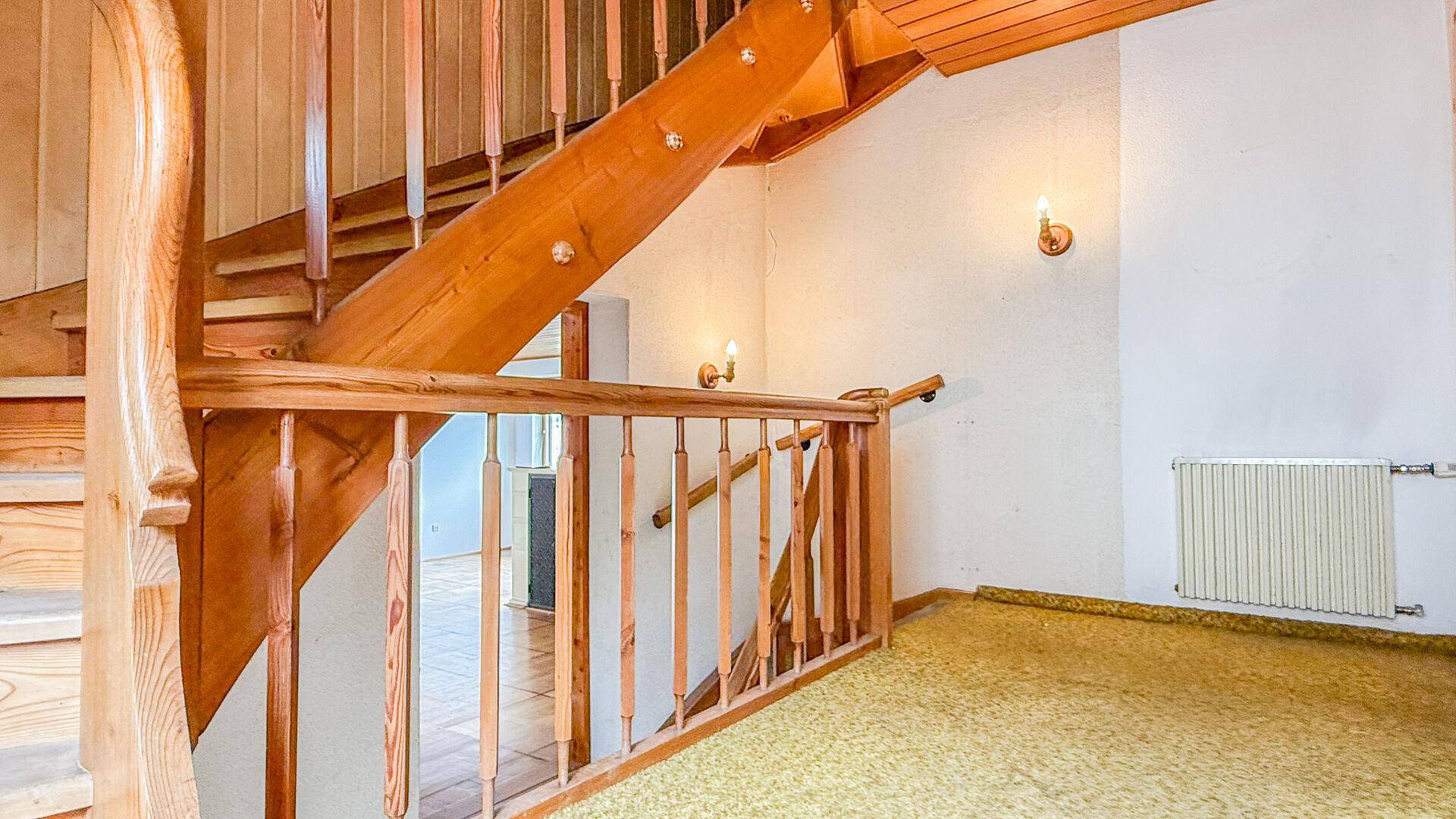 Holztreppe mit gelbem Teppichläufer, die in die obere Etage des Hauses führt.