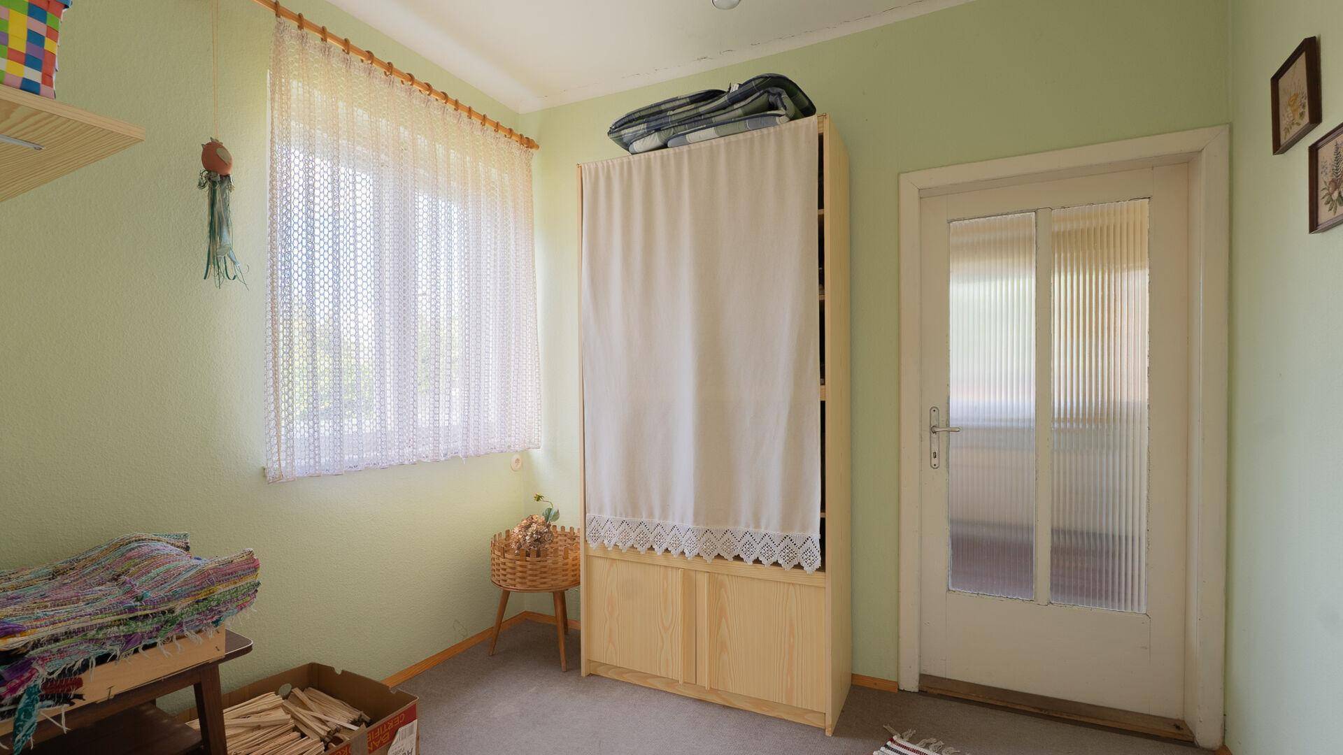 Helles Zimmer mit hellem Schrank, Fenster und einfacher Einrichtung.