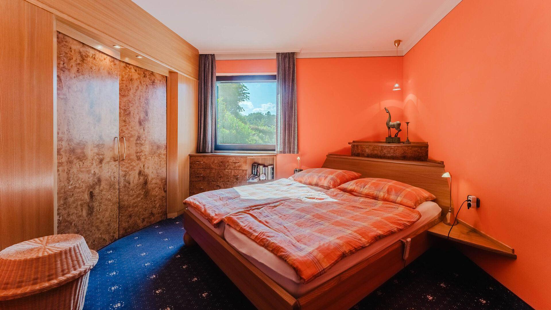 Schlafzimmer mit orangefarbenen Wänden, Doppelbett und Teppichboden.
