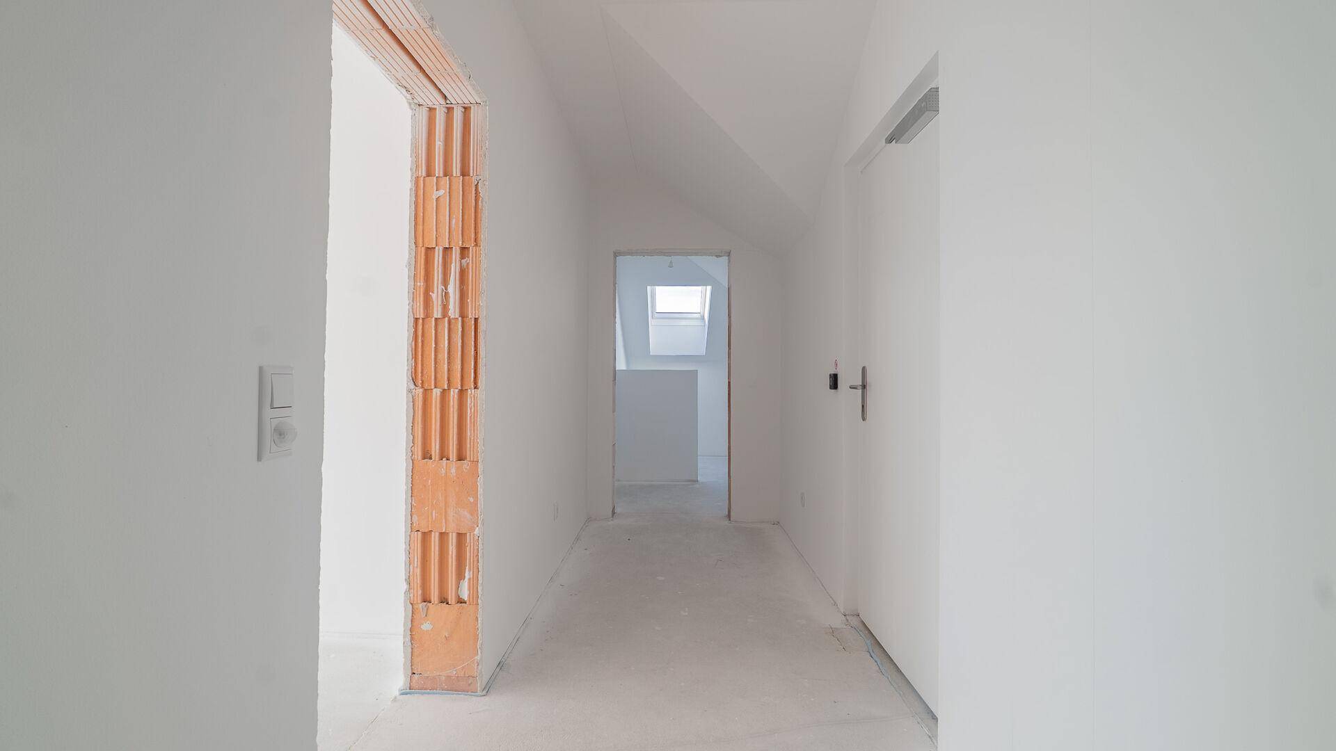 Unfertiger Flur in einem Neubau mit Blick auf ein Dachfenster im Hintergrund.