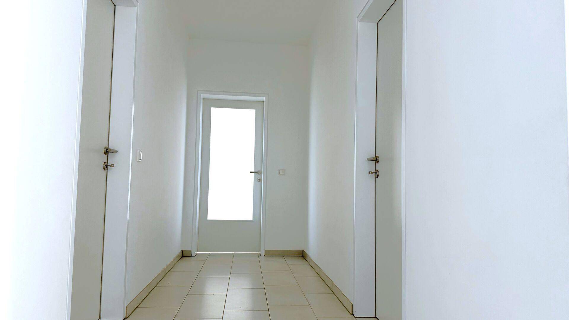 Heller Flur mit Fliesenboden und weißen Wänden, der zu verschiedenen Zimmern führt.