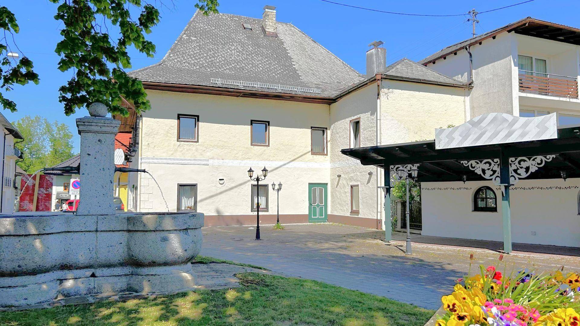 Außenbereich mit Steinbrunnen, gepflastertem Platz und dem historischen Gebäude im Hintergrund.