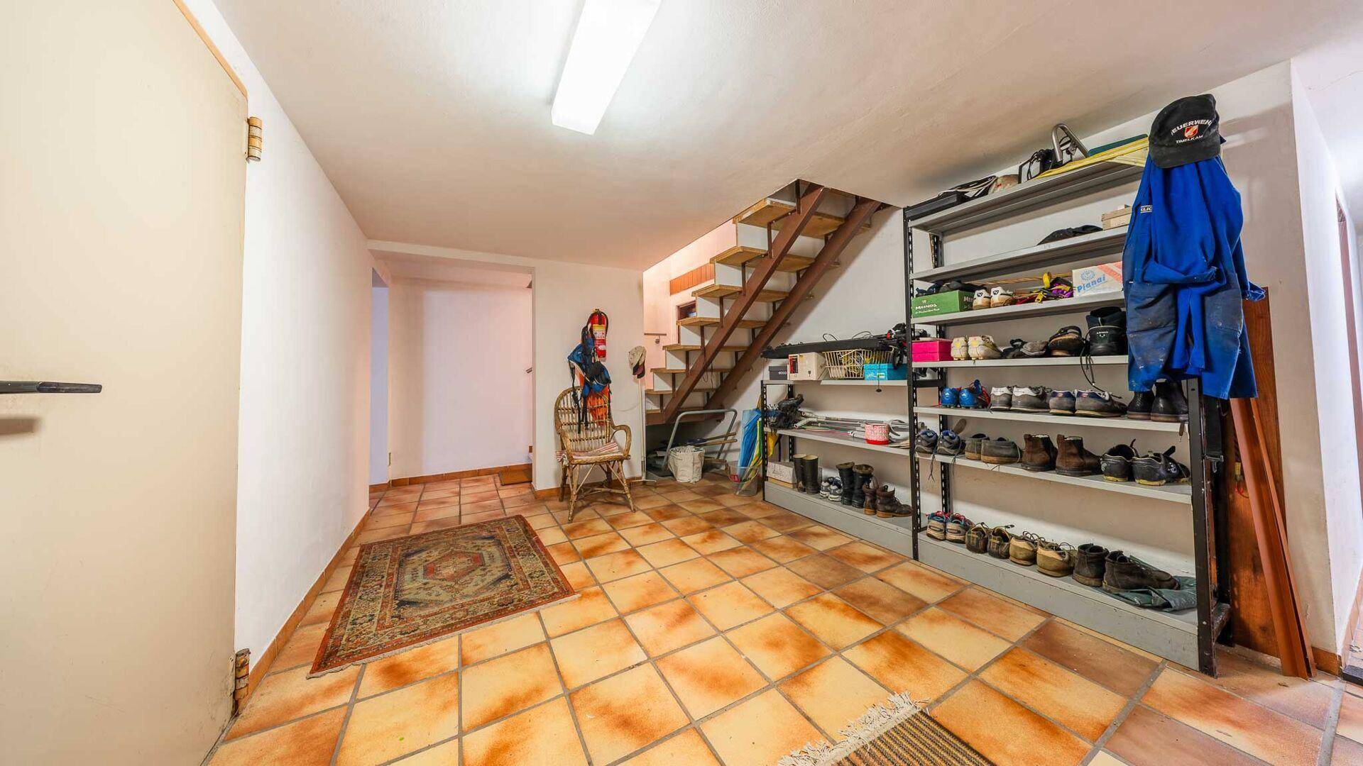 Geräumiger Flur mit gefliestem Boden, offener Treppe und praktischen Regalen für Schuhe und Kleidung.