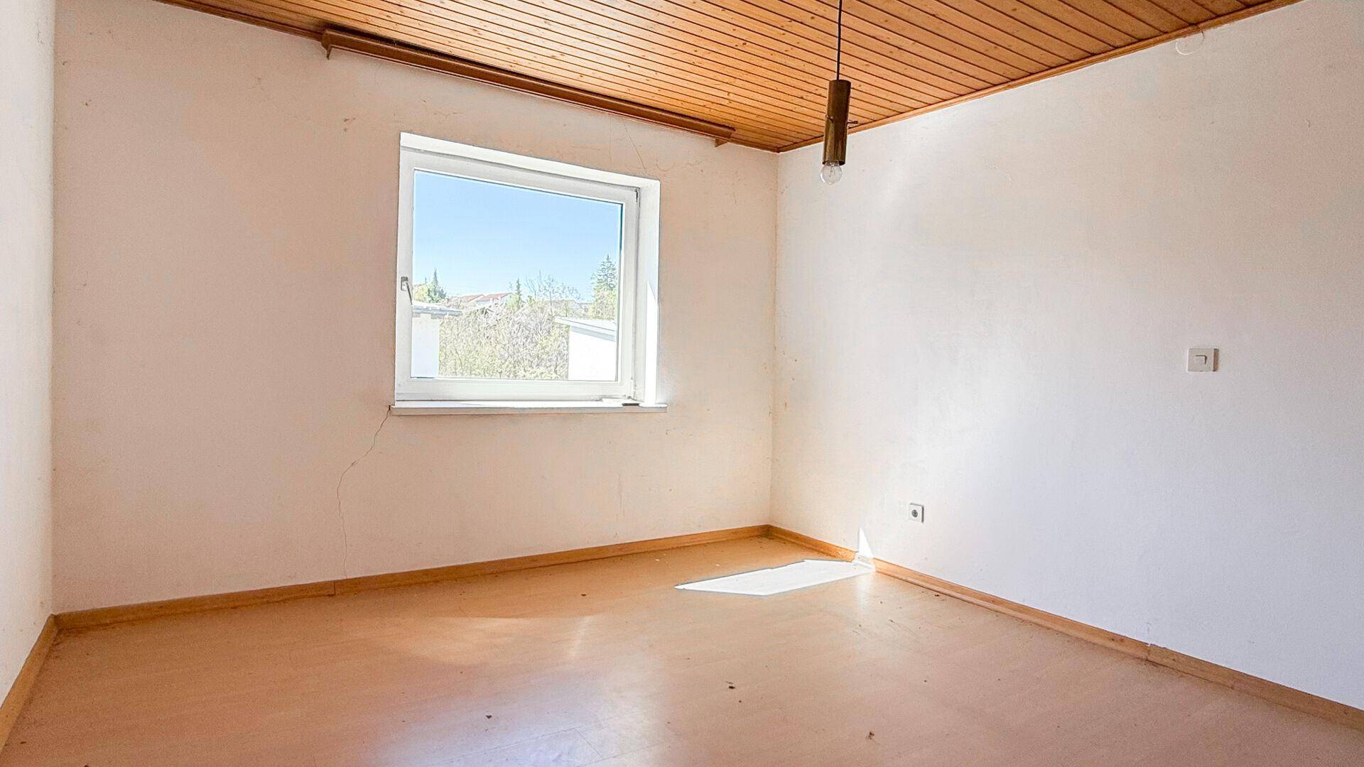 Helles Schlafzimmer mit Holzdecke und Laminatboden, gut belichtet durch ein großes Fenster.