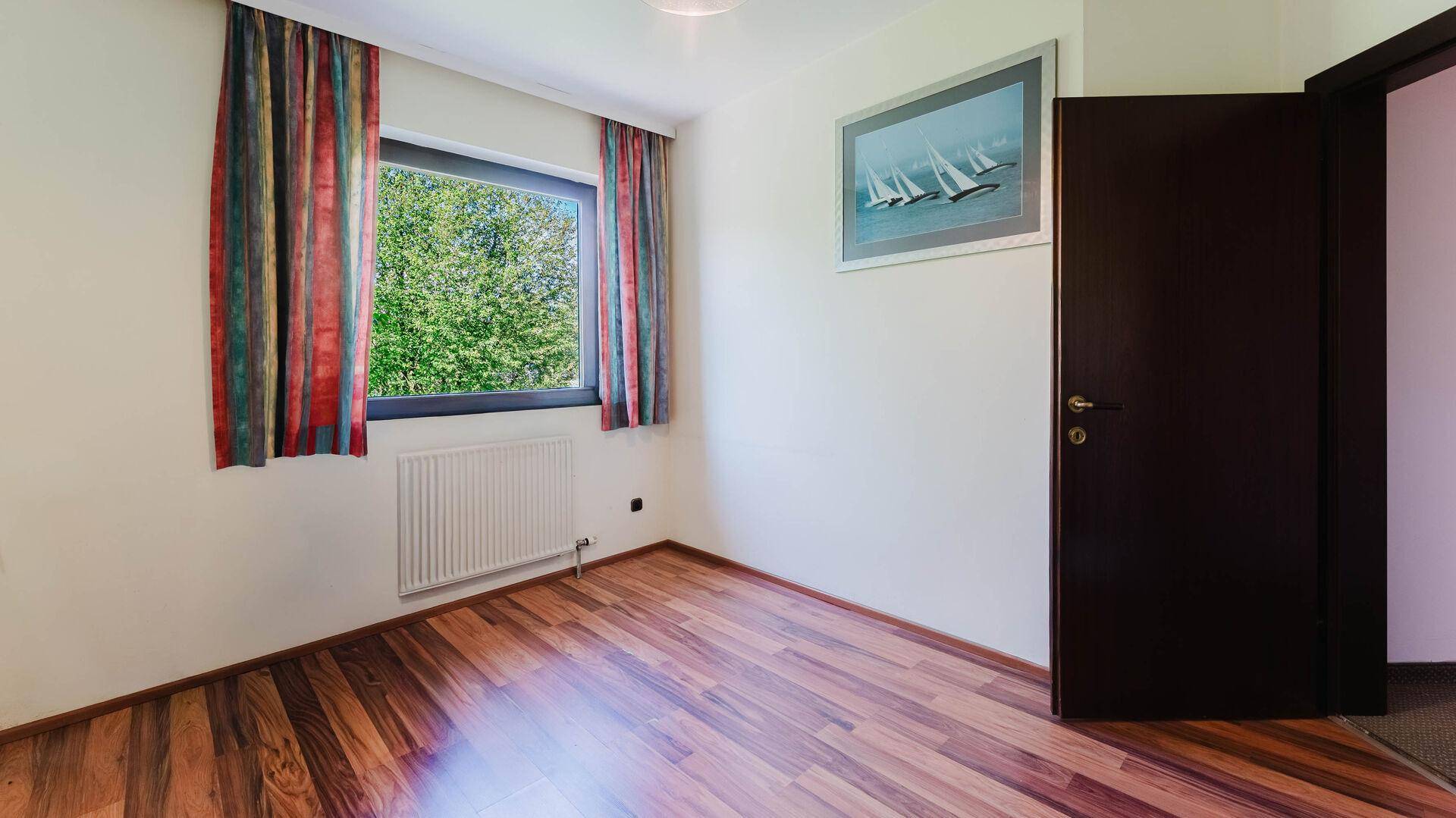 Helles Schlafzimmer mit Holzboden, Fenster und Heizkörper.