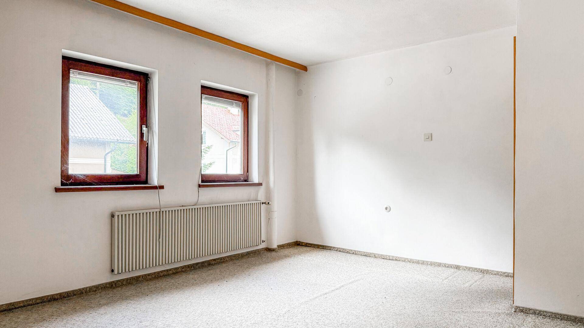 Helles, leeres Zimmer mit zwei Fenstern und einem Teppichboden, der vielseitig nutzbar ist.