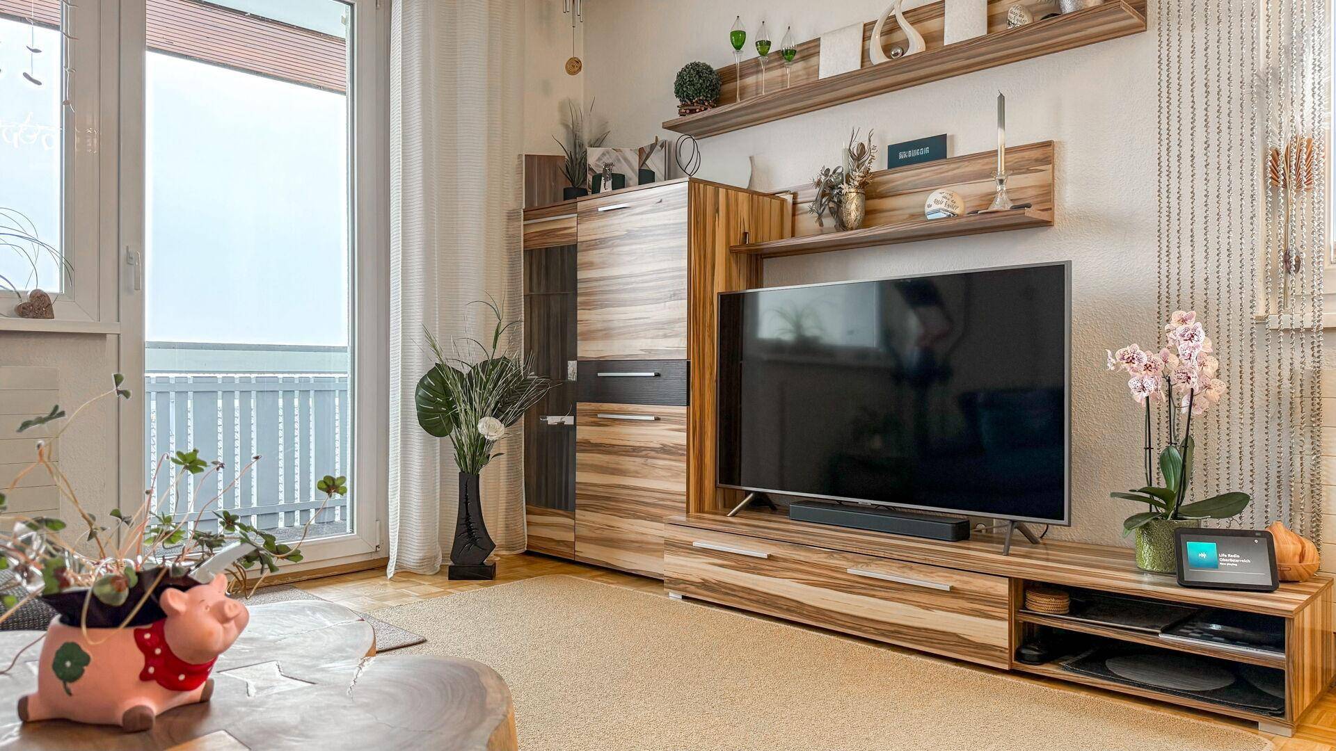 Gemütlicher Wohnbereich mit Holzmöbeln, Fernseher und Blick ins Grüne vom Balkon.