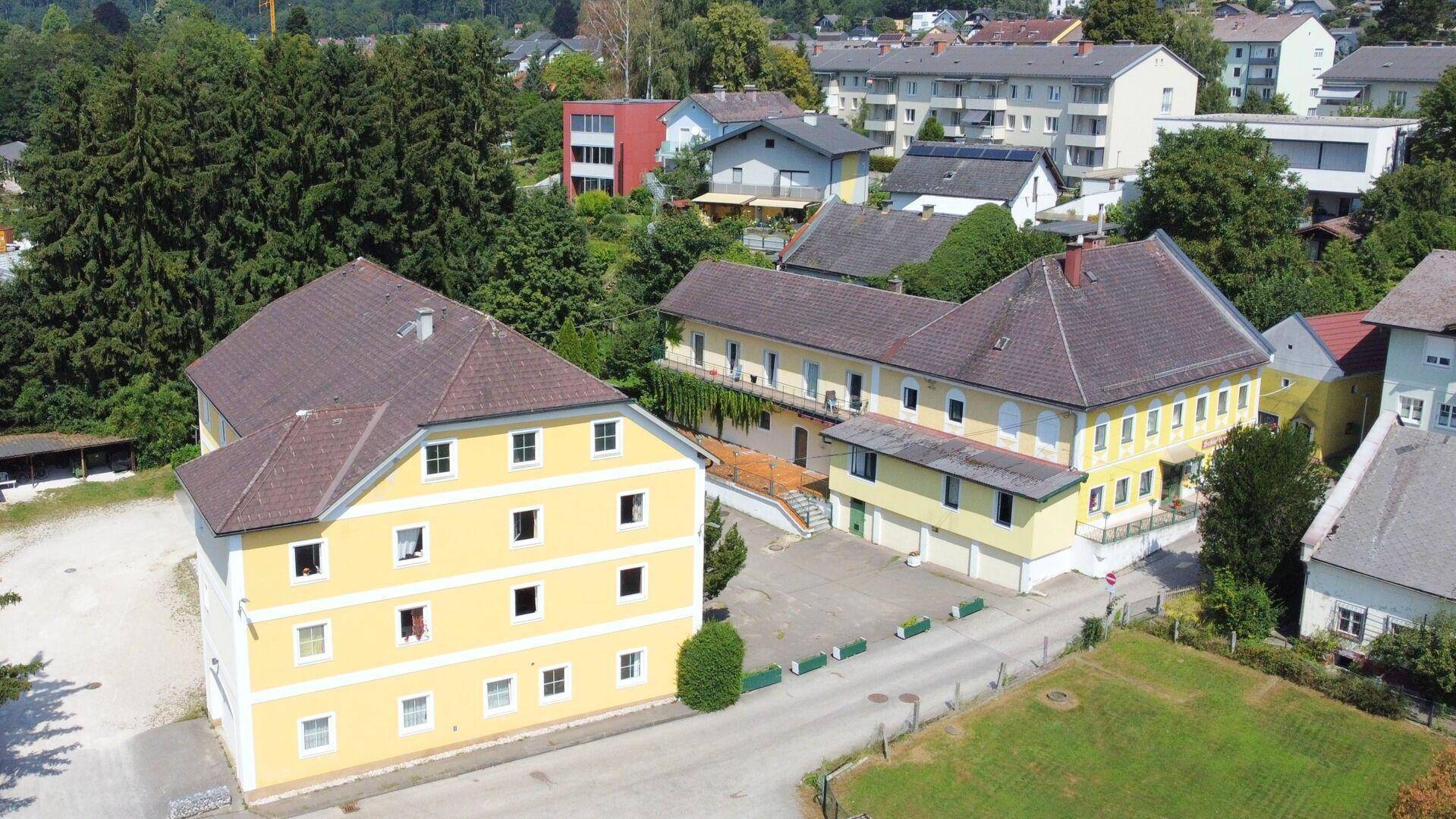 Weitläufige Luftaufnahme des Gebäudekomplexes mit umliegenden Häusern und viel Grün.