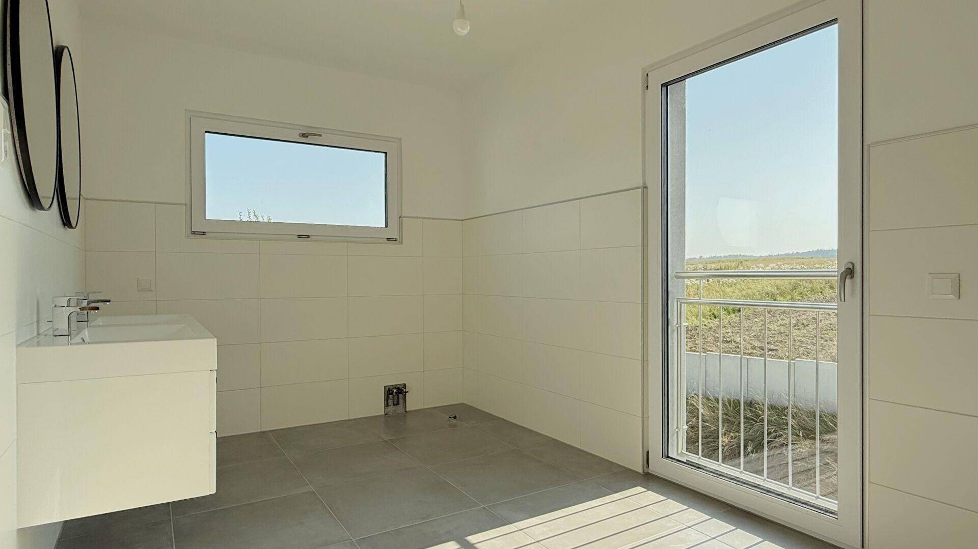 Geräumiges Badezimmer mit Fliesenboden, Fenster und französischem Balkon, bereit für die Installation.