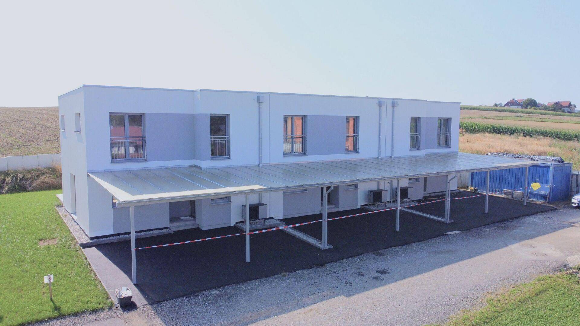 Lange Carport-Anlage vor den Reihenhäusern, die geschützten Parkraum für mehrere Fahrzeuge bietet.