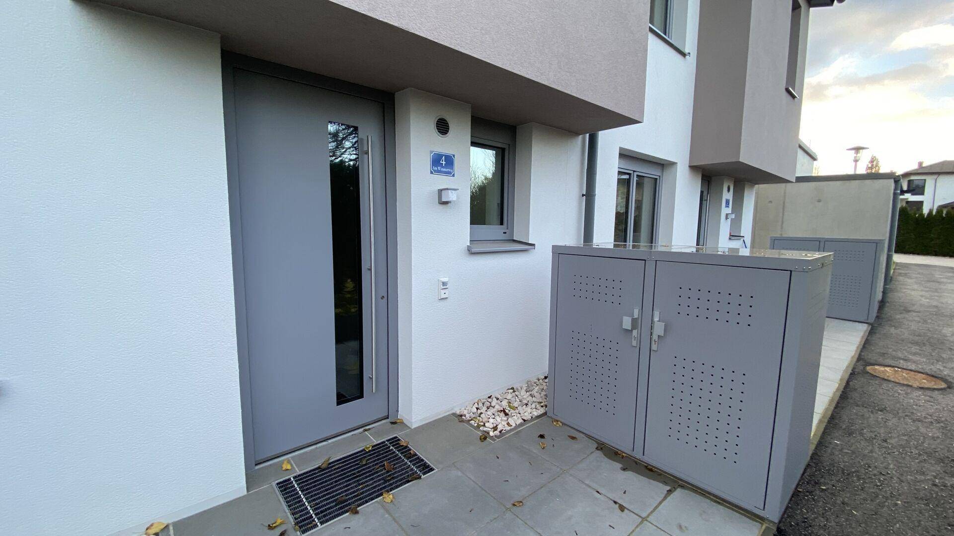 Eingangsbereich eines Reihenhauses mit moderner grauer Tür und praktischen Abstellboxen.