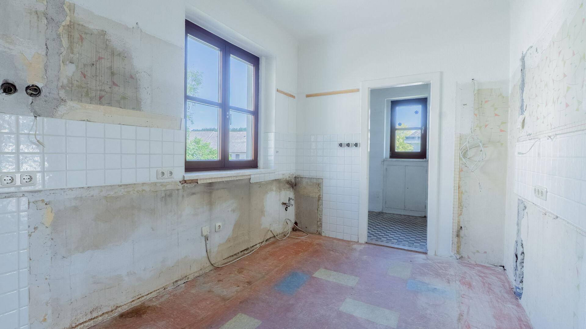 Renovierungsbedürftige Küche mit alten Fliesen und freiliegenden Leitungen.