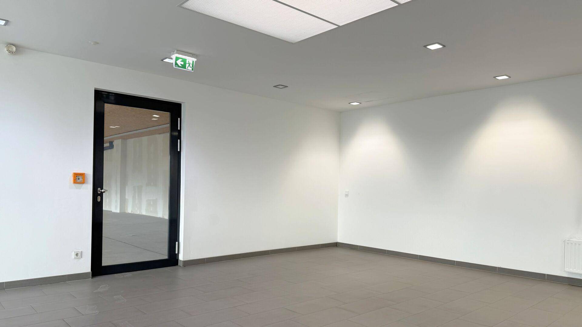 Heller Flur mit weißen Wänden, grauen Fliesen und einer modernen Glastür, ausgestattet mit Deckenleuchten.