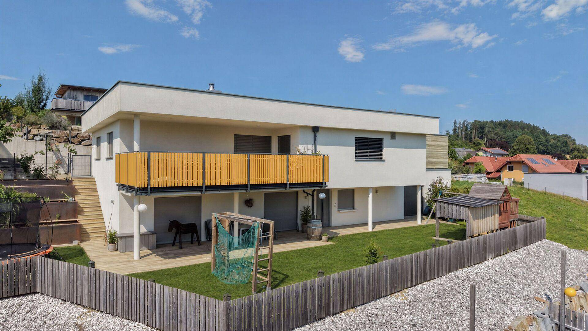 Rückansicht des Hauses mit gepflegtem Rasen, Spielbereich und Balkon mit Holzzaun.
