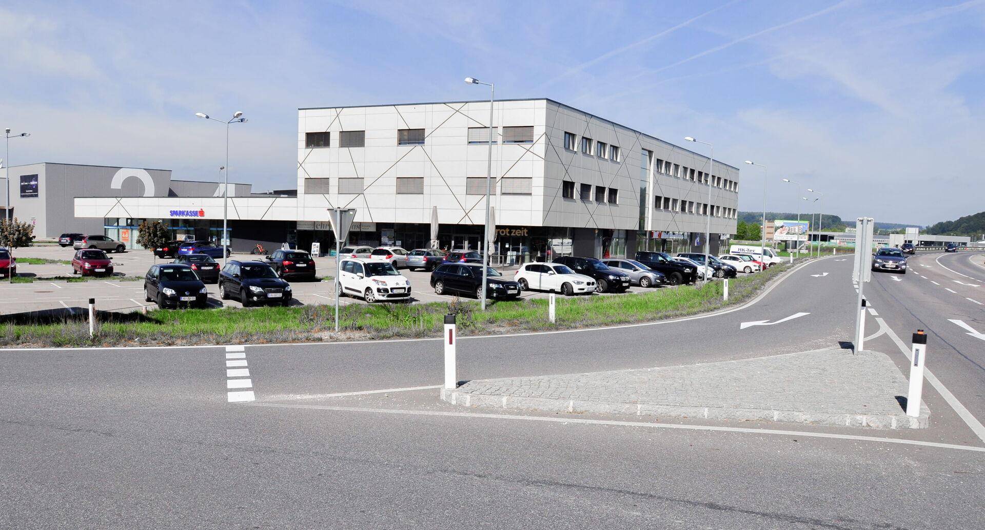 Modernes Geschäftsgebäude an einer Hauptstraße mit zahlreichen Parkplätzen und klarer Zufahrt.