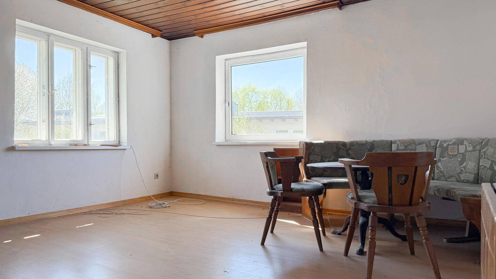 Heller Wohnbereich mit Holztisch, Eckbank und Holzdecke, durch große Fenster gut belichtet.