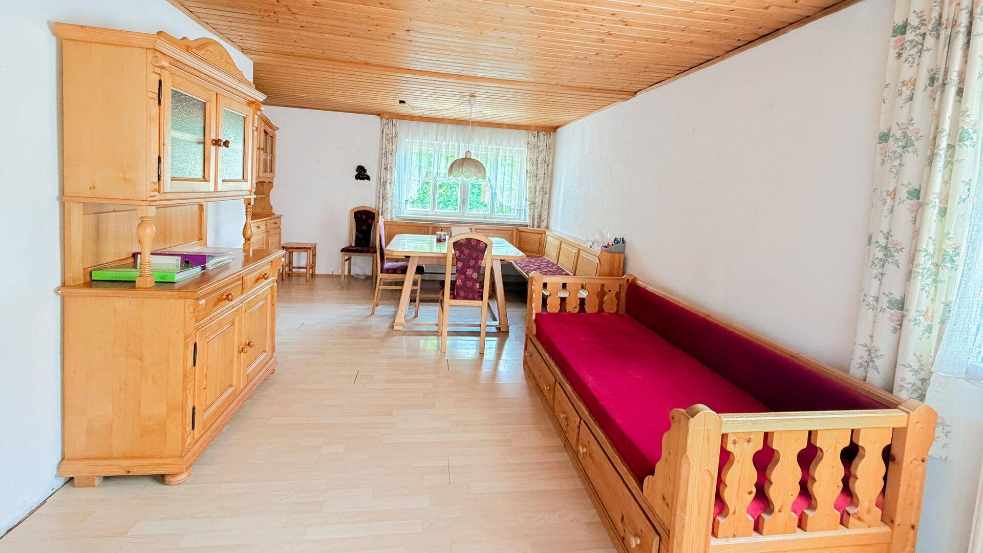 Gemütlicher Wohn-Essbereich mit Holzdecke, traditionellen Holzmöbeln und einem Tagesbett.