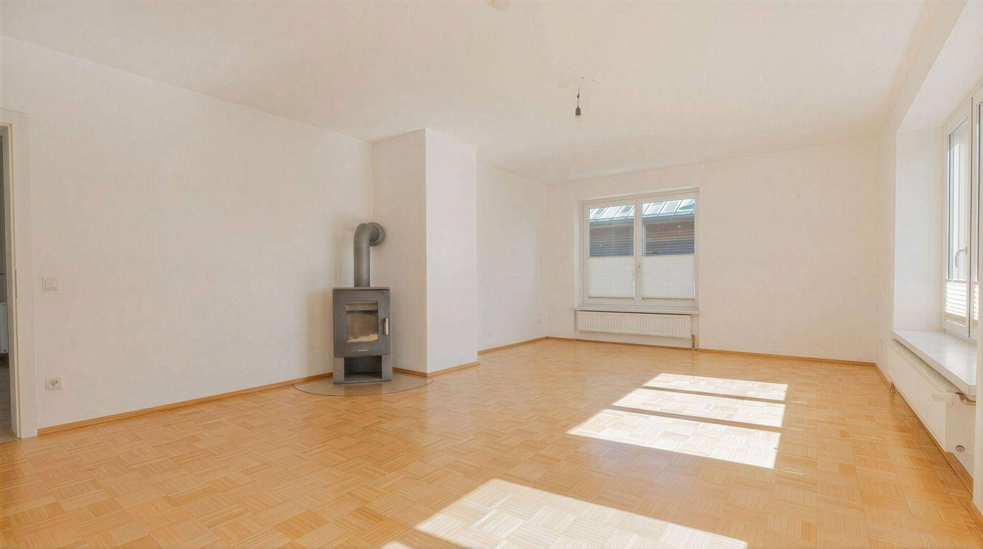 Geräumiges Wohnzimmer mit hellem Parkettboden und einem modernen Kaminofen.