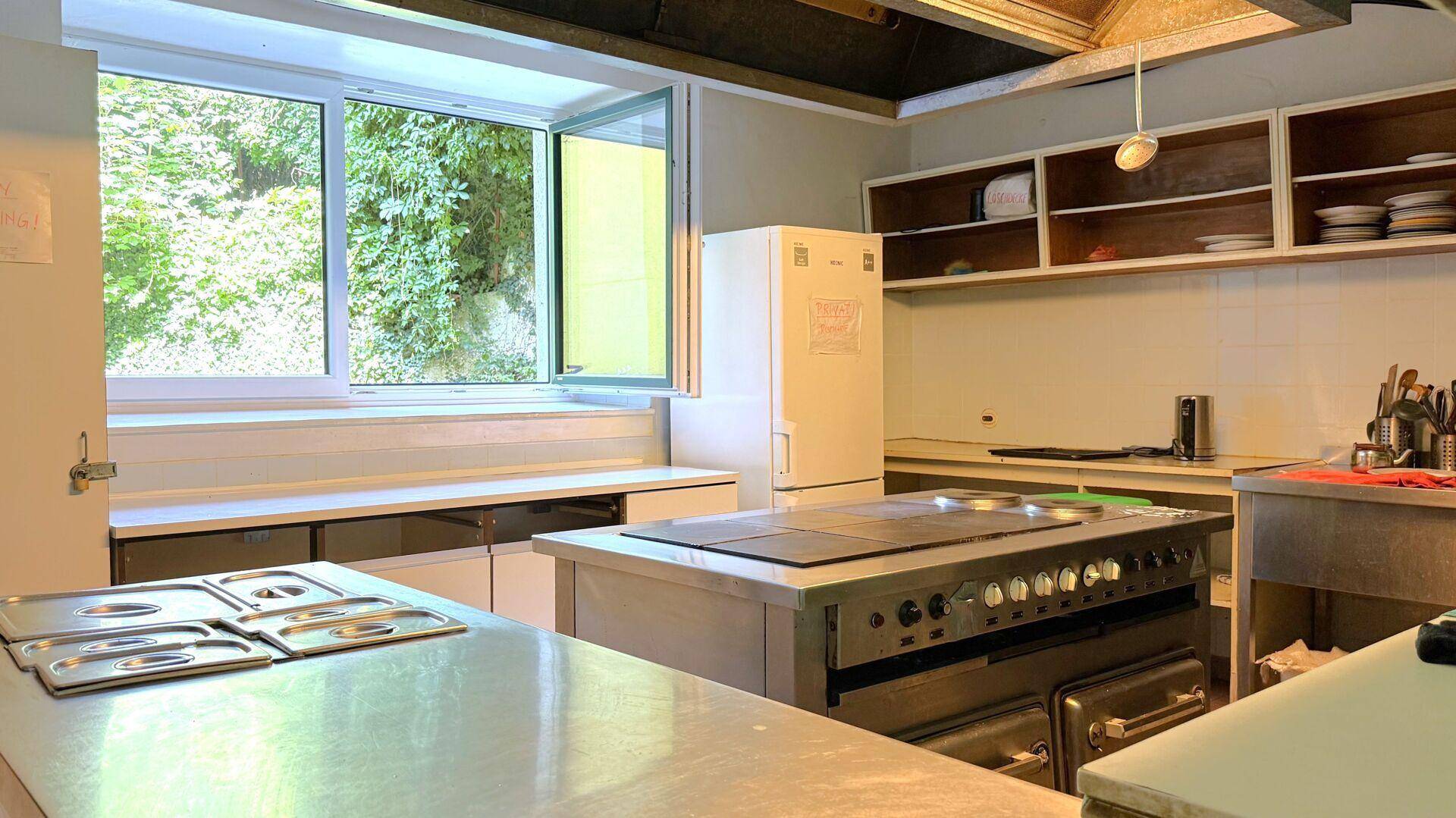 Geräumige Gewerbeküche mit Edelstahlgeräten, großem Fenster und viel Arbeitsfläche.