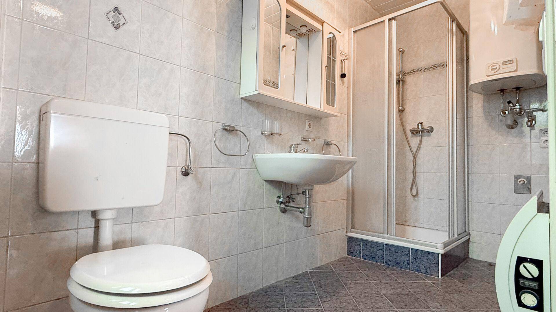 Badezimmer mit Duschkabine, WC und Waschbecken, gefliest in hellen Farbtönen.