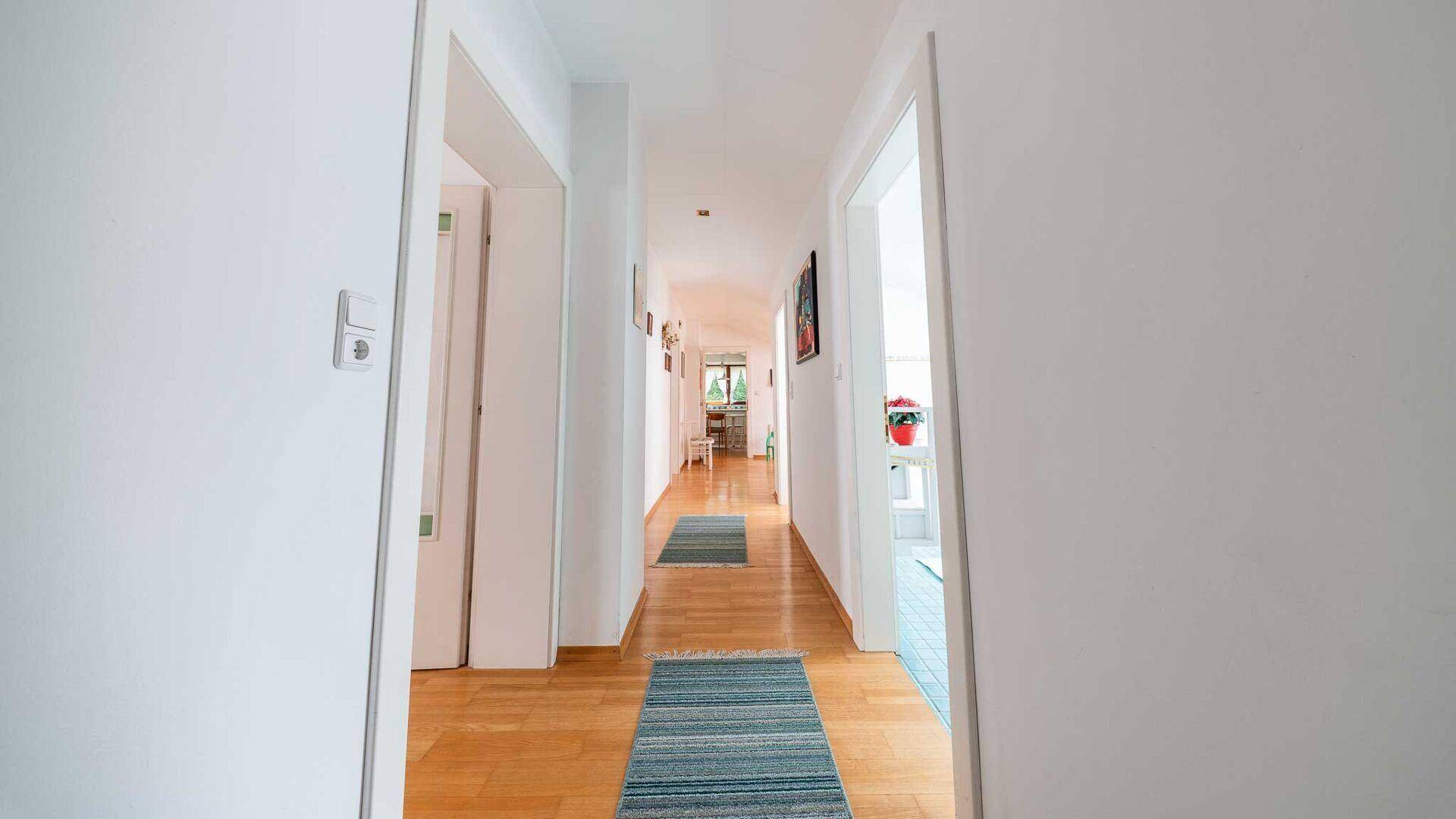 Langer, heller Flur mit Holzparkett, der verschiedene Zimmer miteinander verbindet.